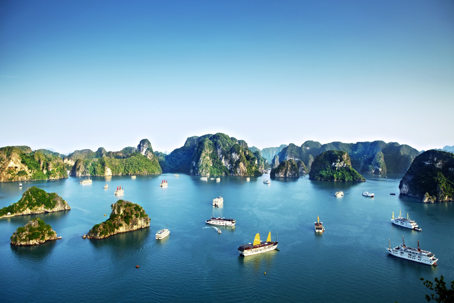 Tour boats and cruise ships passing by limestone islands in Halong Bay.