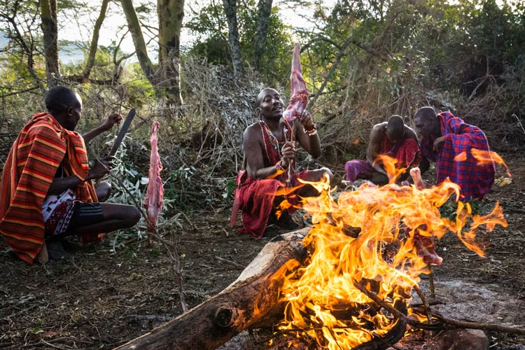 Maasai warriors prepare to roast meat over an open fire. Image by Michael Benanav / Lonely Planet.