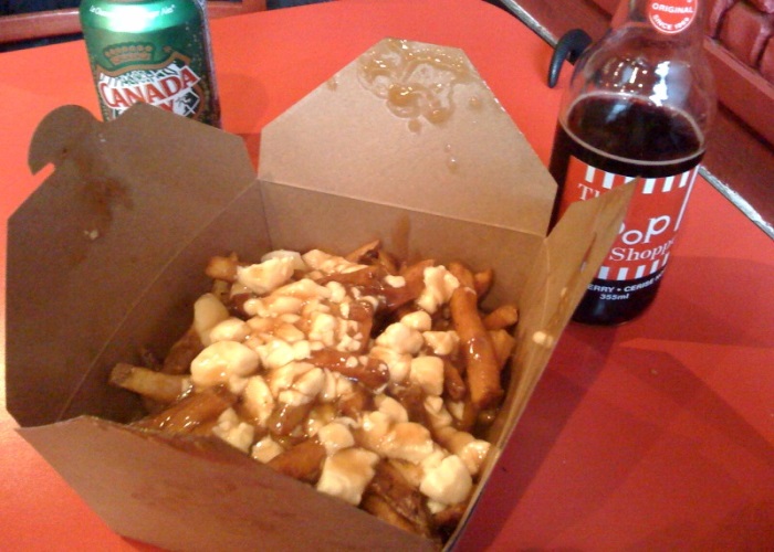 A carton of poutine with a can of Canada Dry on the side