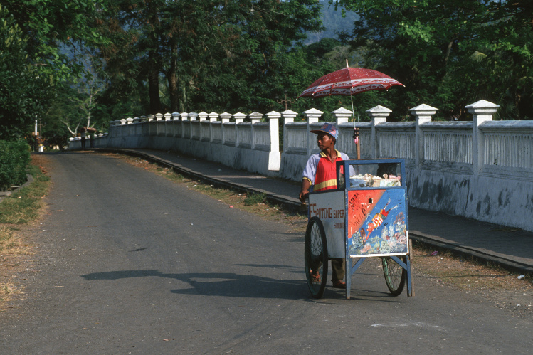 A food vendor pushes his food cart along a sleepy street in the Spice Islands. Image by Peter Charlesworth