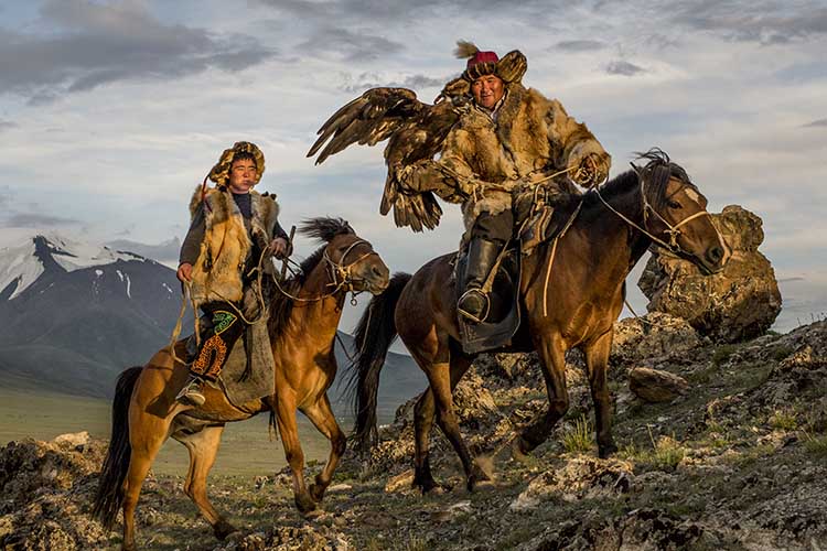 Hunters Silou and his son Berik climb a ridge with their eagle. Image by David Baxendale / Lonely Planet