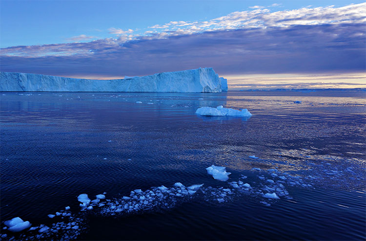 A bright blue section of the Jakobshavn glacier is lit up by the midnight sun in Greenland, while the dark blue sea surrounding it is sprinkled with tiny chunks of ice