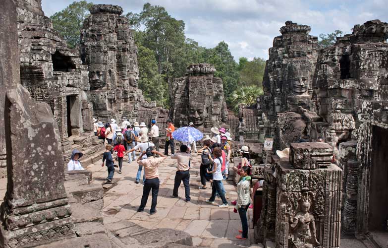 Tourists at the Bayon, Angkor Thom, Siem Reap, Cambodia. Image by Andrew Stewart  / Robert Harding World Imagery / Getty Images .
