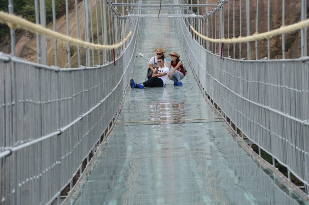 Tourists walk on the 300-metre suspension bridge made of glass at the Shiniuzhai National Geological Park, China. ...