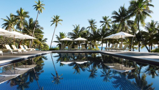 Sun loungers and parasols by a pool under palm trees, Vomo Island, Mamanuca Islands.