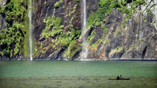 A tourist kayaks past waterfalls in Milford Sound.