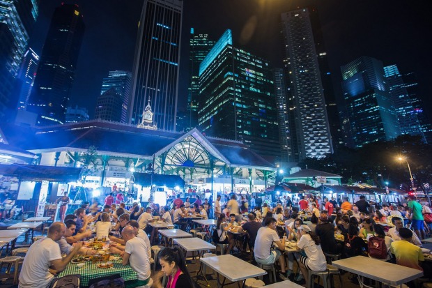 Diners sit at restaurant tables at the Lau Pa Sat food court as commercial buildings stand illuminated at night in the ...