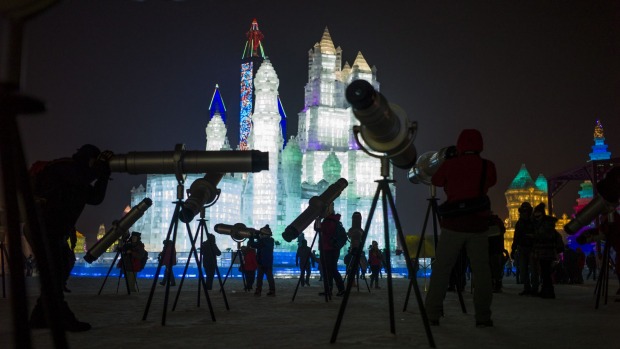 People look through telescopes of ice sculptures illuminated by coloured lights during the opening day of the Harbin ...