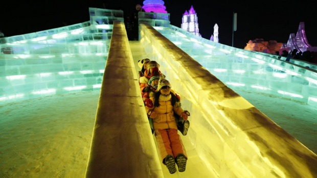 Children ride a slide on ice sculptures illuminated by coloured lights during the opening day of the Harbin ...