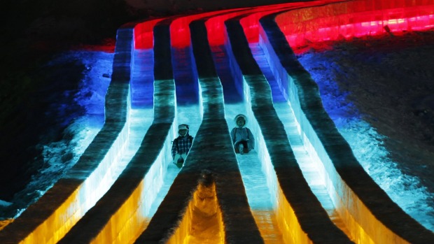 People ride slides on ice sculptures illuminated by coloured lights during the opening day of the Harbin International ...