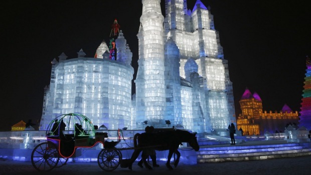 Tourists sit on a horse-drawn carriage in front of ice sculptures illuminated by coloured lights.