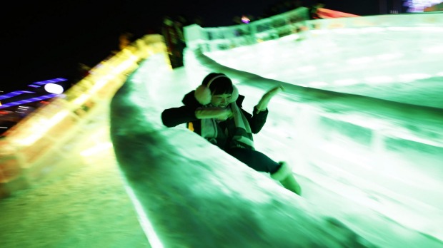 A woman rides a slide on ice sculptures illuminated by coloured lights during the Harbin International Ice and Snow ...
