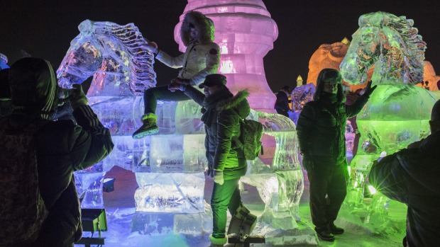 Visitors take photographs on an ice sculpture during the Harbin International Ice and Snow Festival in Harbin, northeast ...