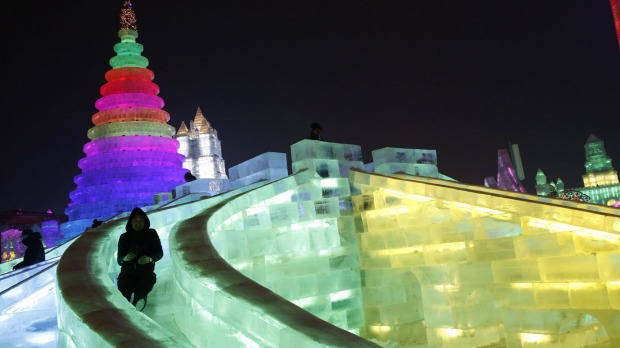 A man rides a slide on an ice sculpture illuminated by coloured lights on the eve of the opening ceremony of the Harbin ...