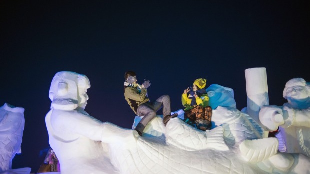 A couple takes pictures on a snow sculpture during the Harbin International Ice and Snow Festival in Harbin, northeast ...