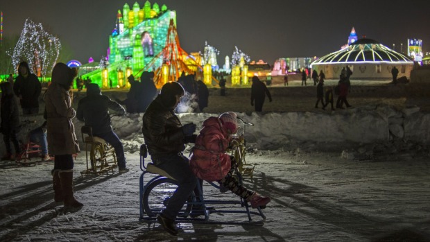 A father and his daughter ride a cycle over ice during the Harbin International Ice and Snow Festival in Harbin, ...
