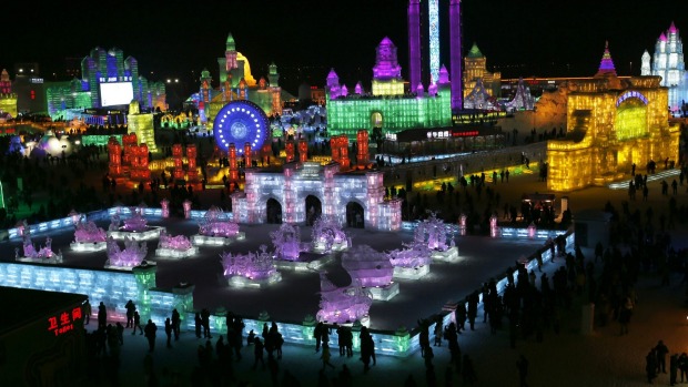 People visit ice sculptures illuminated by coloured lights during the opening day of the Harbin International Ice and ...