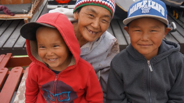 Painting break: Inuit grandmother with two children take a break from painting their dog sled.