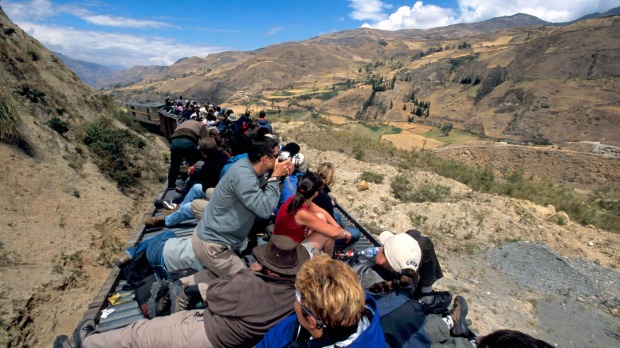 Tourists and locals onboard the Devil's Nose Railway train sit on the top of the rail cars travelling through the mountains.