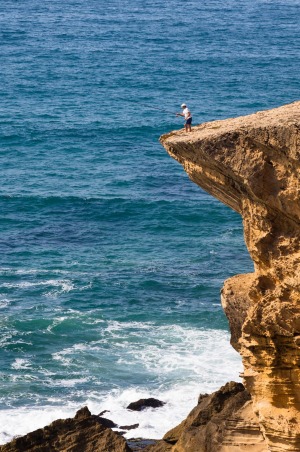 Fisherman on a cliff at Monte Clerigo Beach, Atlantic Coast, Algarve.