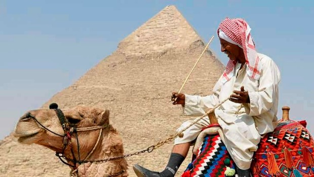 A guide waits for tourist to take them for a ride on his camel in front of the Great Pyramid of Giza.