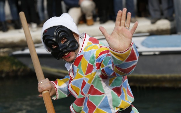 A man dressed as Arlecchino (Harlequin) waves as he rows a boat during the water parade, part of the Venice Carnival, in ...