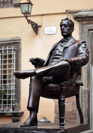Giacomo Puccini is depicted in his birthplace, Lucca, holding his omnipresent cigar.