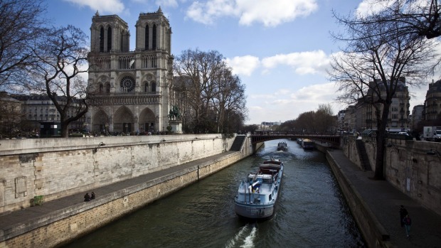 A river barge carries cargo along the River Seine and past the Notre Dame cathedral in Paris.