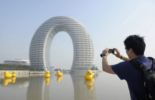 A man takes pictures of the Sheraton Huzhou Hot Spring Resort, or Moon Hotel, behind replicas of the rubber duck by ...
