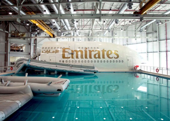 Aircraft emergency escape chutes extend into the training pool, next to an Emirates Airline simulator.