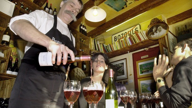 A cafe owner pours wine for his customers in the very different drinking culture of Paris.