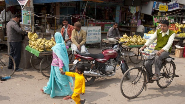 Pedestrians and a bicyclist pass fruit vendors on a New Delhi street.