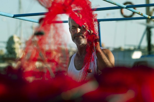 A patient fisherman combs his nets for knots and debris in the late afternoon on the docks of the small village of ...