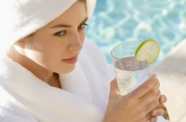 woman in white bathrobe sipping iced water by a pool
