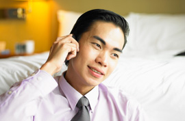 asian man on cell phone sitting in front of a bed