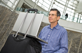 man in an airport using his laptop that he has placed on top of his suitcase