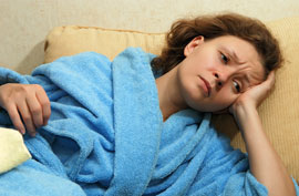 women in blue bathrobe lying down with look of pain on her face
