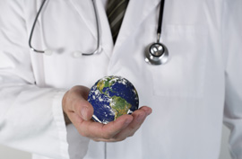 A doctor with a stethoscope around his neck holding a small planet earth globe in his hand.