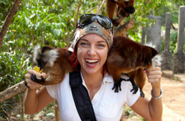 A woman in a white shirt and bandana with two lemus on her shoulders eating food from her hands.